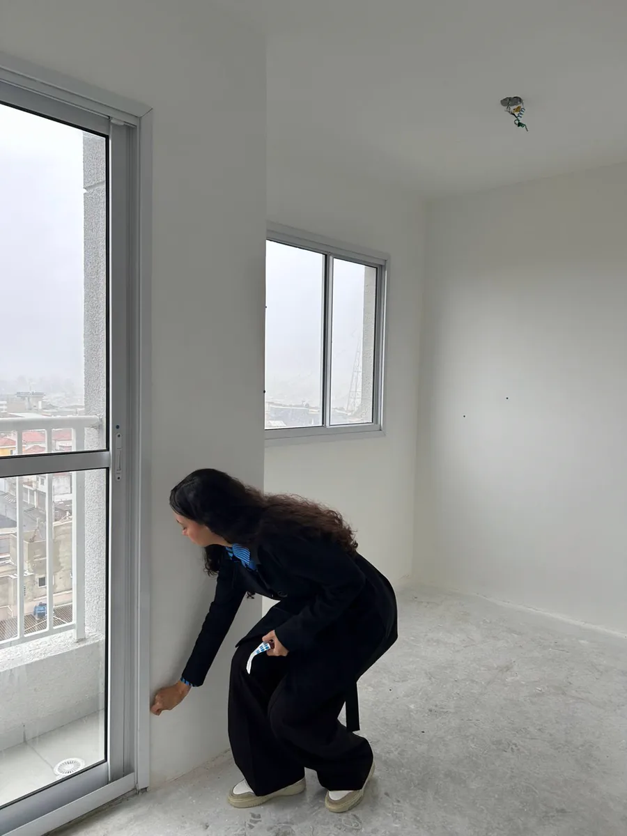 Bianca conferindo o encaixe da esquadria de uma porta de sacada em um apartamento novo ainda sem acabamento.