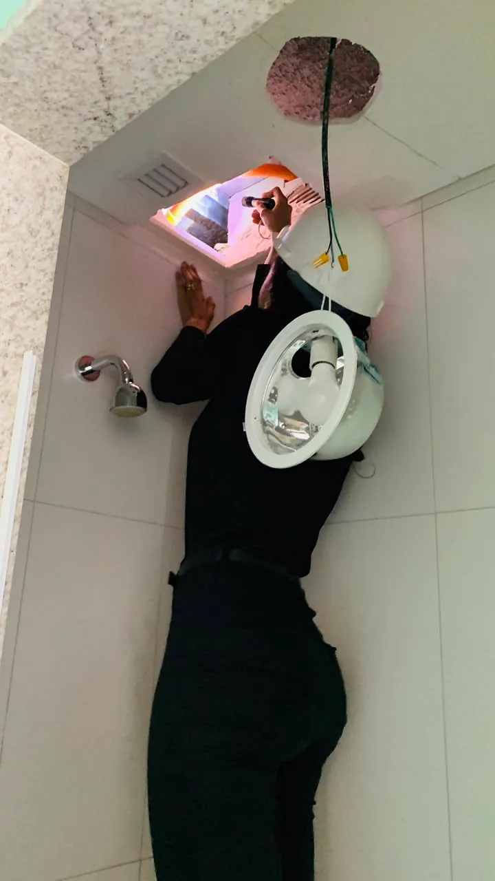 Inspeção com lanterna do interior do forro de um banheiro, com a luminária removida.