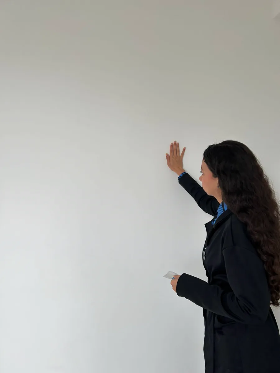 Bianca conferindo o acabamento de uma parede branca em um apartamento recém-entregue.